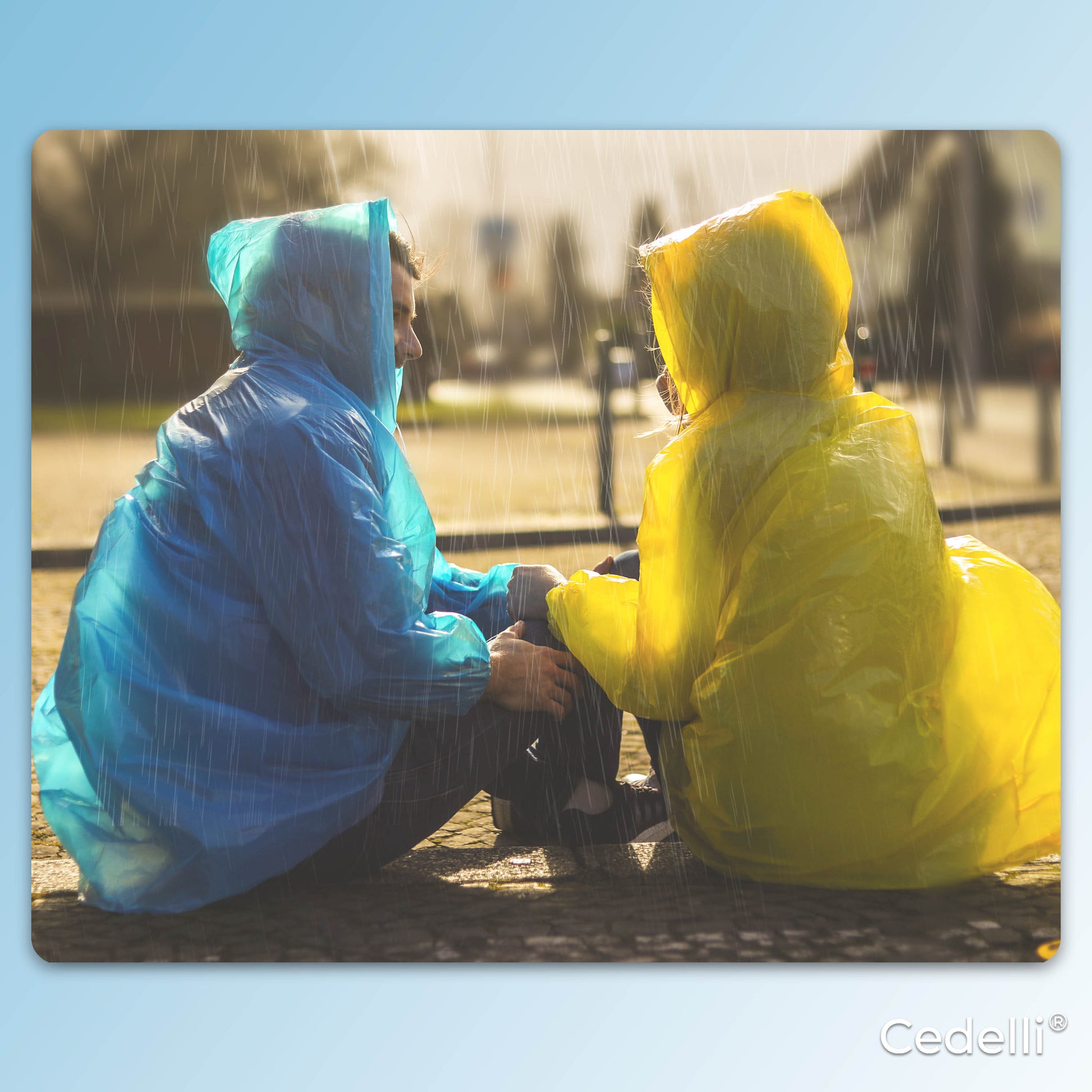 Zwei Personen in gelbem und blauem Cedelli Regenponcho sitzen im Regen – ideal für Outdoor-Abenteuer